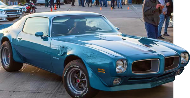 Classic blue Pontiac Firebird parked outside JBA Speed Shop during a car event, showcasing custom performance tuning and restoration work.