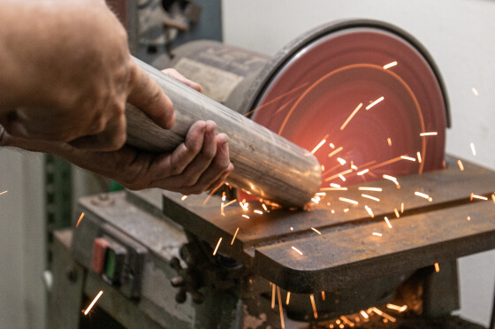 A JBA technician sanding down a pipe with sparks flying for custom fabrication
